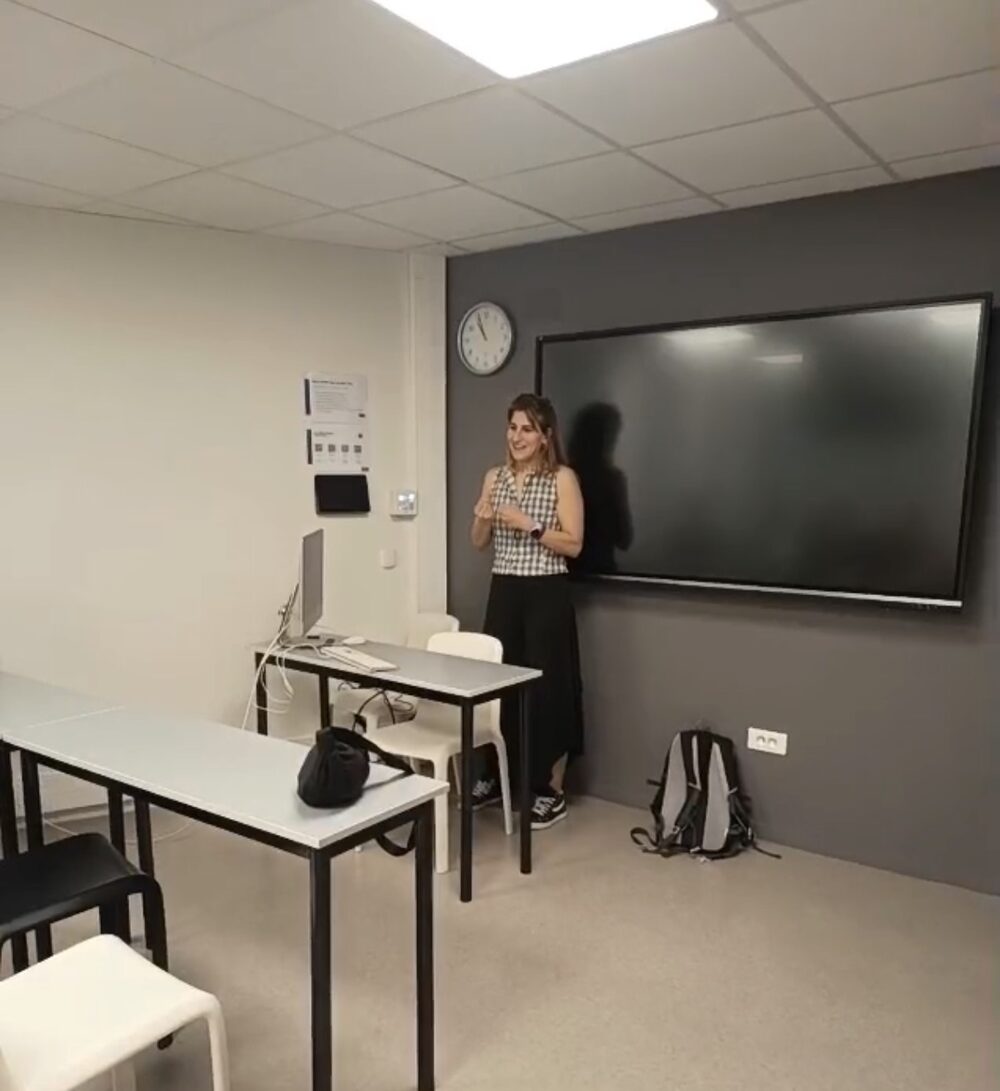 Titania Blesh standing and speaking in the ISCOM classroom during the session